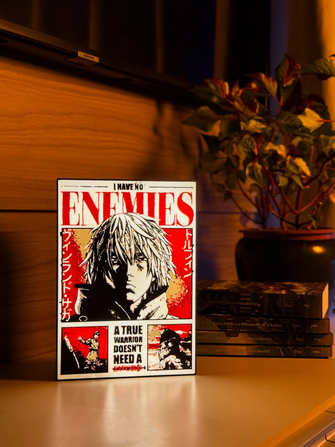 Luminária I Have No Enemies acesa em estante de sala com planta e livros